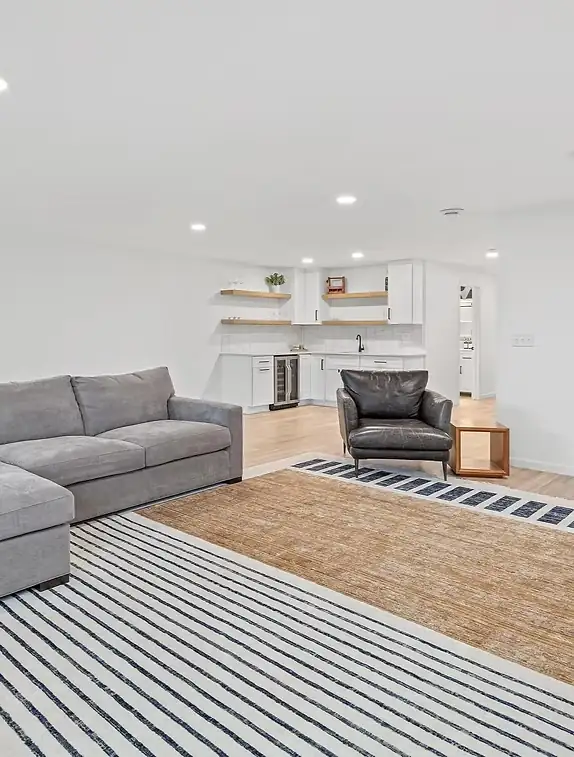 Finished basement with a sectional sofa, wet bar with white cabinets, open shelves and wood-look floor