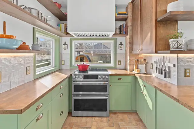 St. Paul Garden Cottage kitchen with green cabinets, wood floating shelves, handmade tile and brick floor