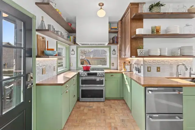Garden Cottage kitchen in St. Paul with sage green cabinets, butcher block counters, open shelves and brick floor