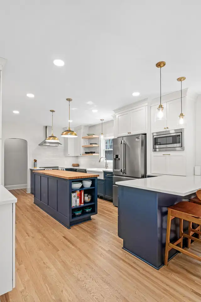 White kitchen in St. Paul with two navy islands, a wood butcher-block top, brass pendants and oak floors