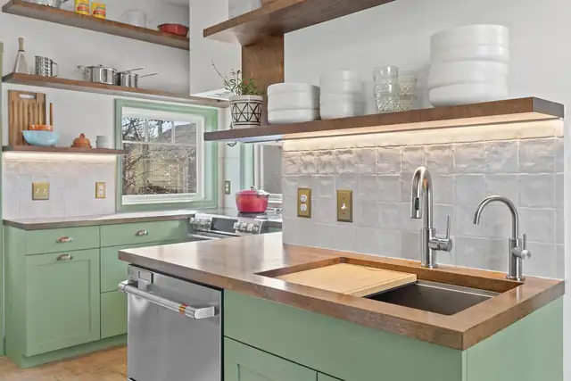 Kitchen by Red Fox with sage green cabinets, a wood-topped island, open wood shelving and a textured tile backsplash