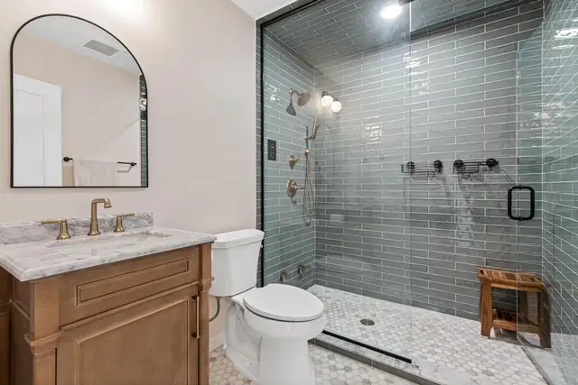 Bathroom with a wood vanity, marble top, arched mirror and a large glass shower with gray glass subway tile and teak bench
