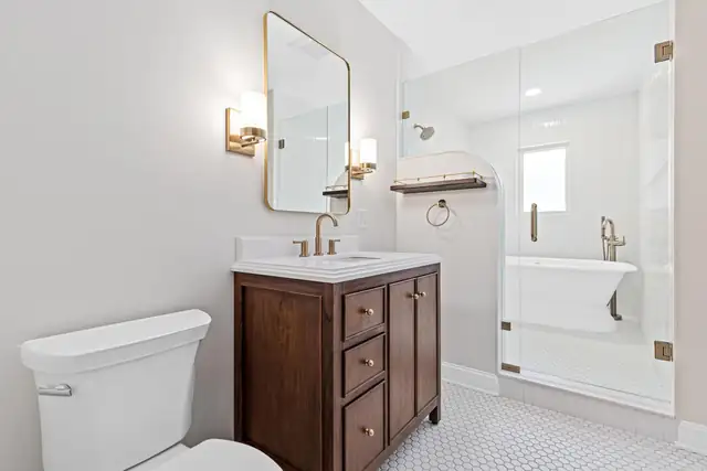 Family bathroom in a historic St. Paul home with walnut vanity, brass fixtures and a freestanding tub in a glass wet room