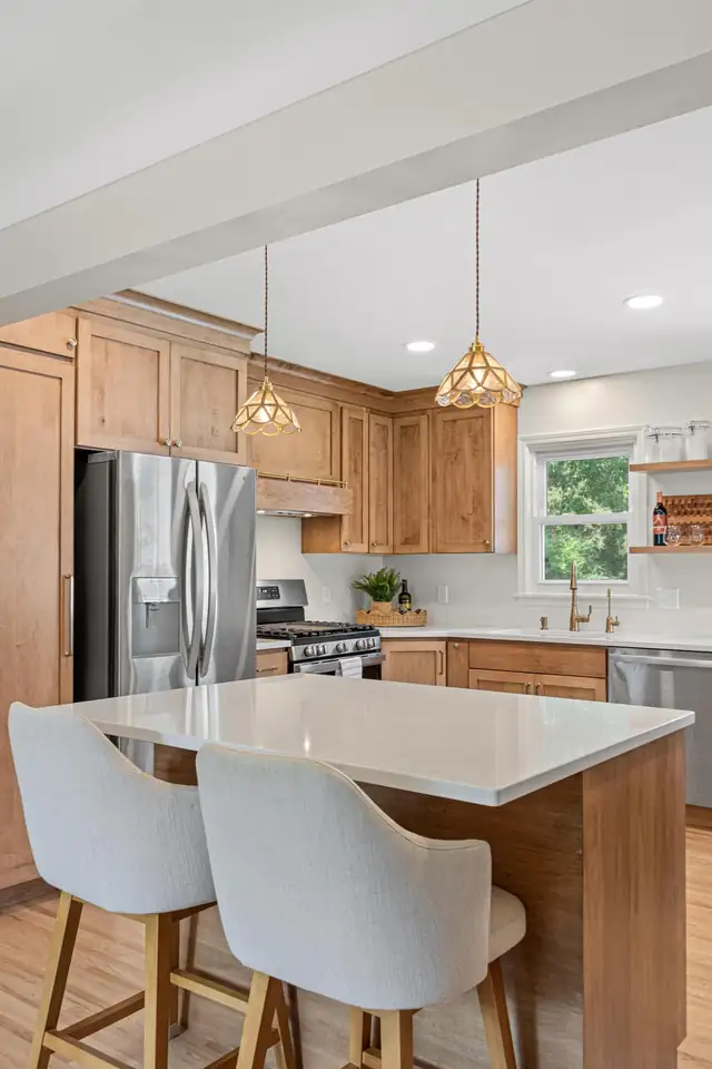 Kitchen with natural wood cabinets, a quartz island, glass pendant lights and a stainless refrigerator